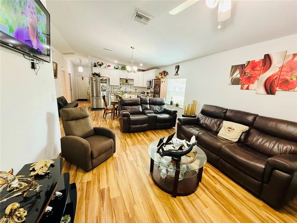 Living room with light wood-style flooring, vaulted ceiling, and ceiling fan