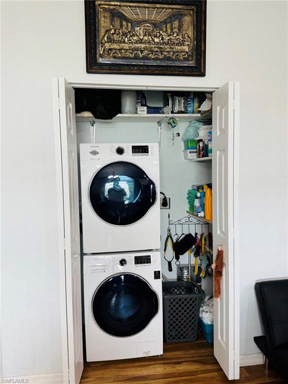 Laundry room with stacked washing machine and dryer and wood finished floors