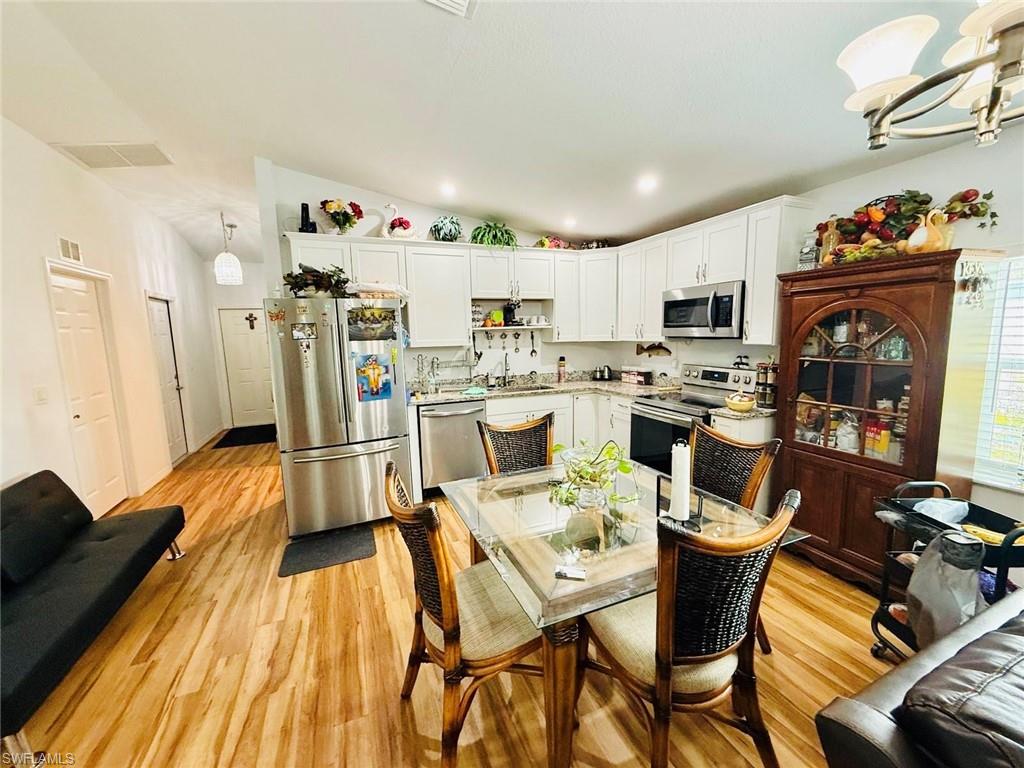 Kitchen featuring stainless steel appliances, white cabinetry, a chandelier, light wood-type flooring, and lofted ceiling