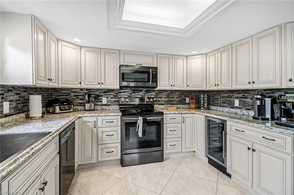 Kitchen with light marble finish floors, stainless steel appliances, light stone countertops, beverage cooler, and a raised ceiling