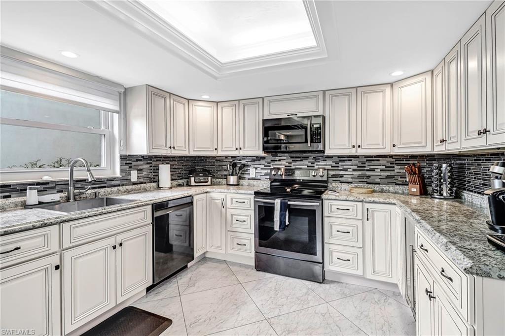Kitchen with appliances with stainless steel finishes, light marble finish floors, light stone counters, a tray ceiling, and recessed lighting