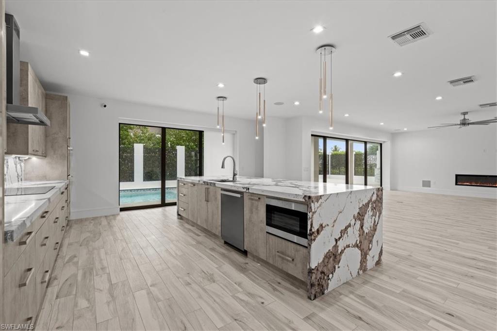 Kitchen featuring healthy amount of natural light, hanging light fixtures, light stone countertops, a spacious island, and recessed lighting