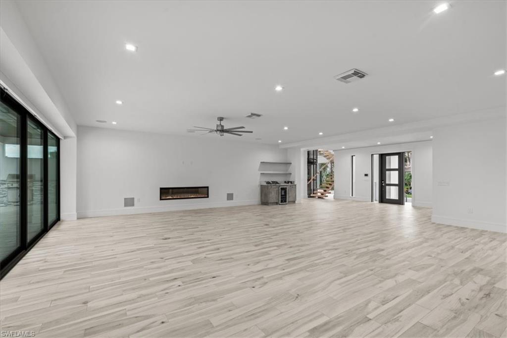 Unfurnished living room featuring a glass covered fireplace, light wood-style floors, recessed lighting, ceiling fan, and french doors