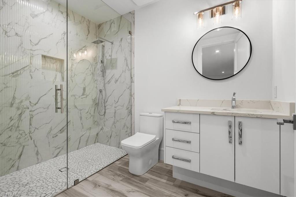 Bathroom featuring vanity, a marble finish shower, and light wood finished floors