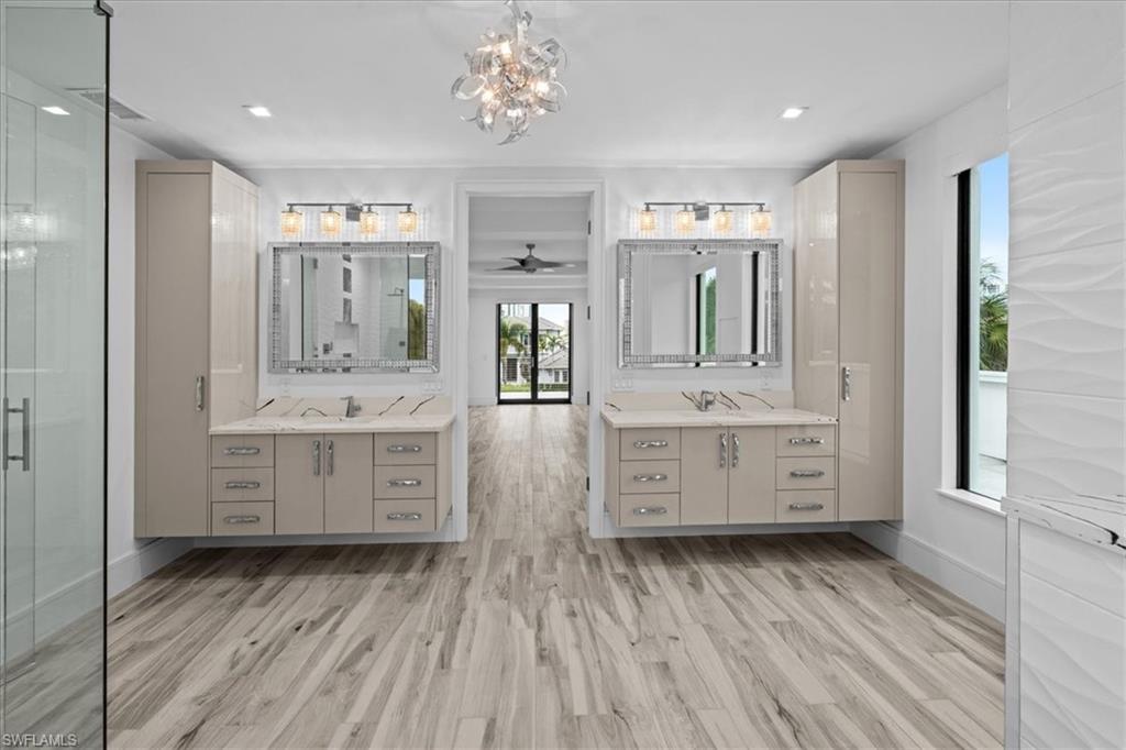 Bathroom with two vanities, light wood-style flooring, a chandelier, and a shower stall
