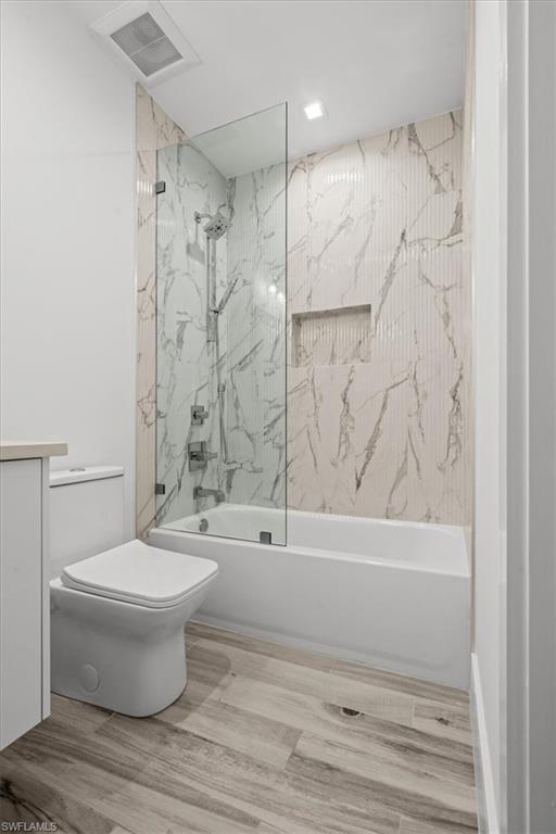 Bathroom with a combined bath / shower with marble appearance, wood finished floors, and vanity
