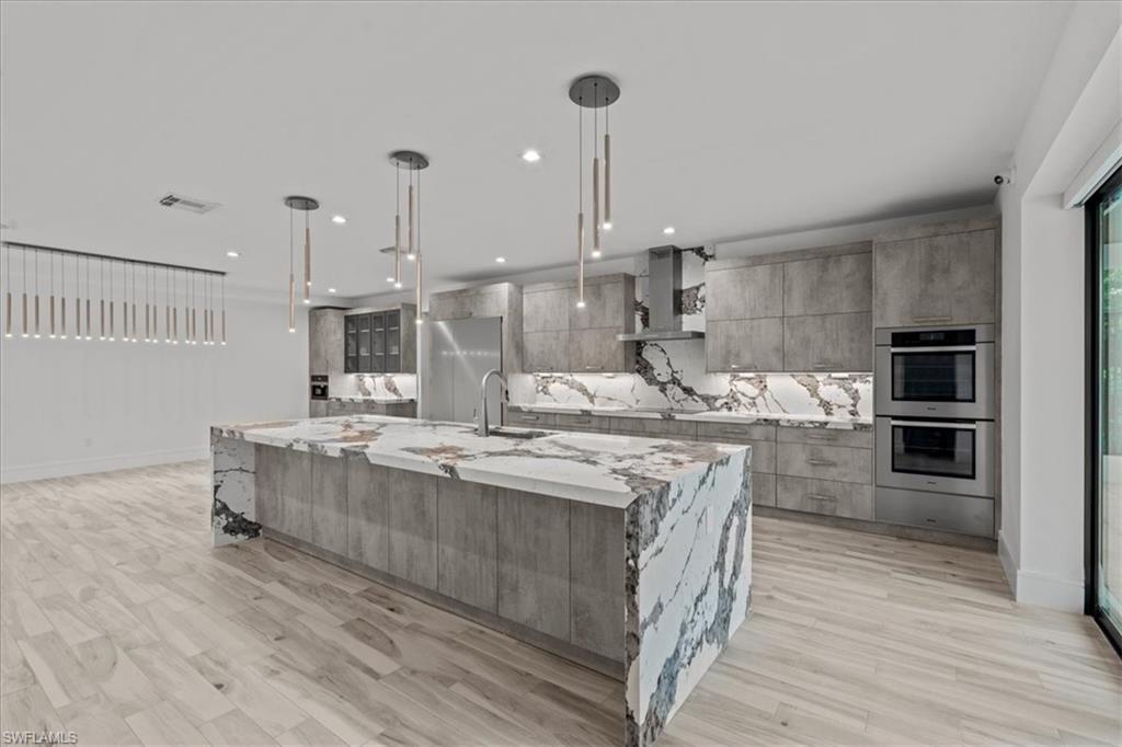 Kitchen featuring tasteful backsplash, modern cabinets, a spacious island, light stone counters, and recessed lighting