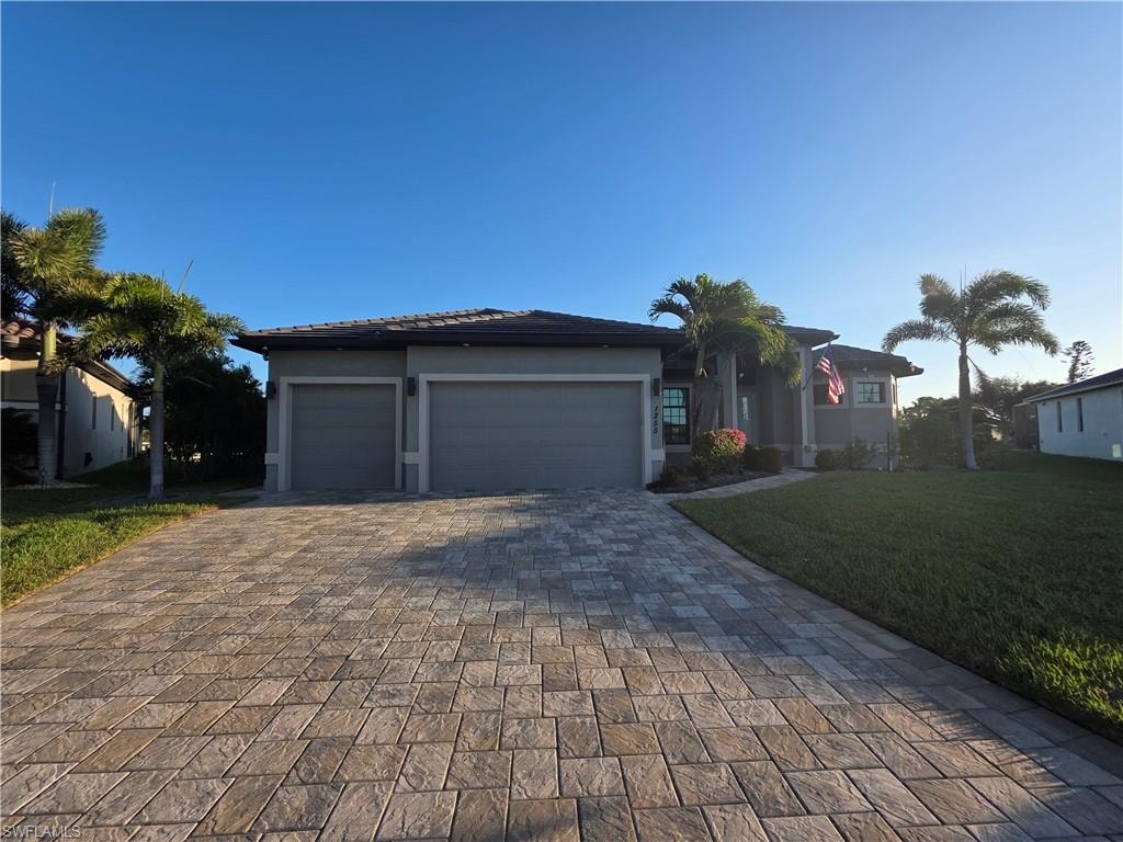 View of front of property featuring a front lawn, a garage, decorative driveway, and stucco siding