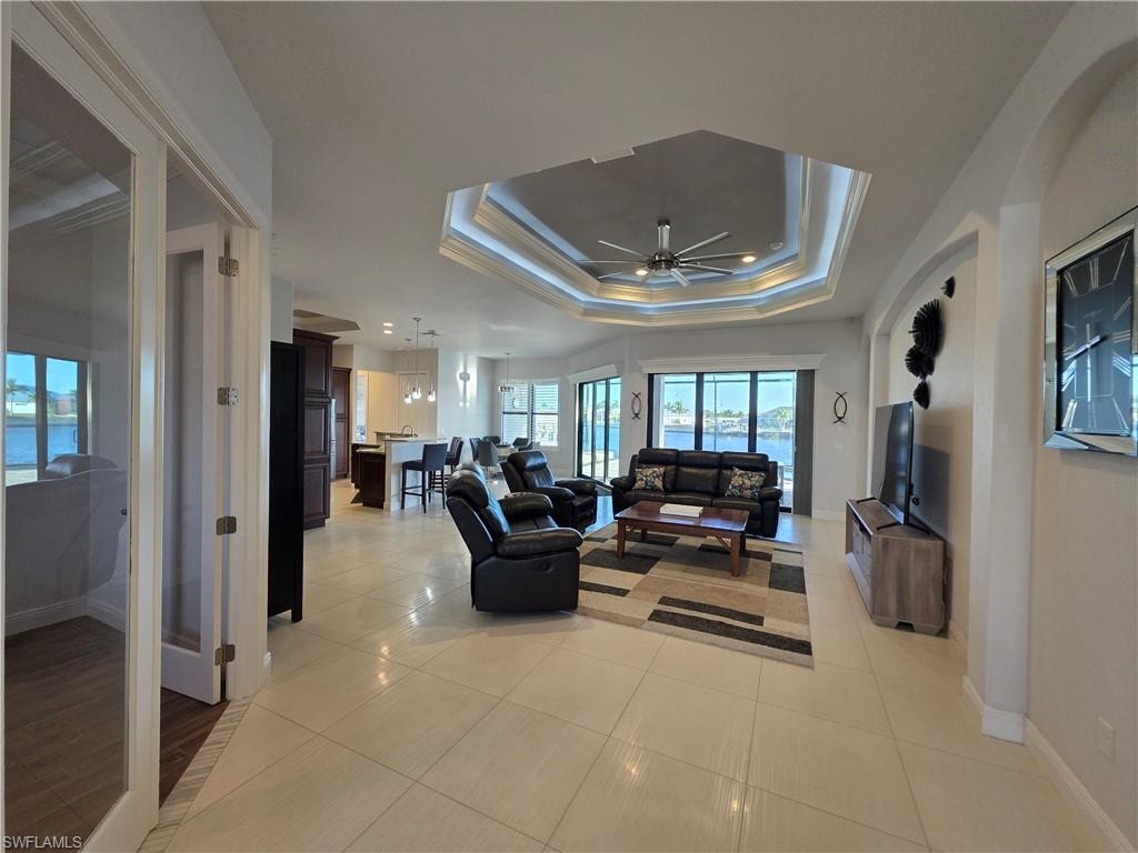 Living room featuring ceiling fan, ornamental molding, light tile patterned floors, and a raised ceiling