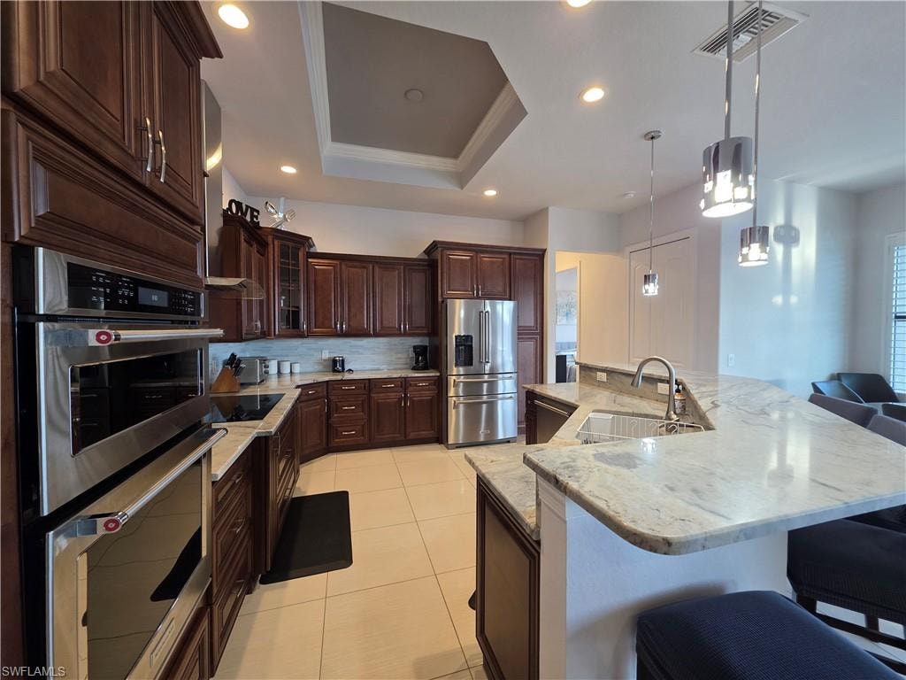 Kitchen with stainless steel appliances, a tray ceiling, a spacious island, a breakfast bar area, and crown molding
