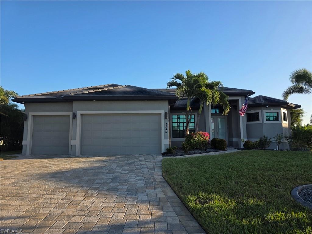 Prairie-style home with decorative driveway, a tiled roof, an attached garage, a front yard, and stucco siding