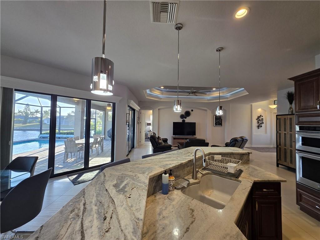 Kitchen with light stone countertops, dark brown cabinets, a raised ceiling, pendant lighting, and open floor plan