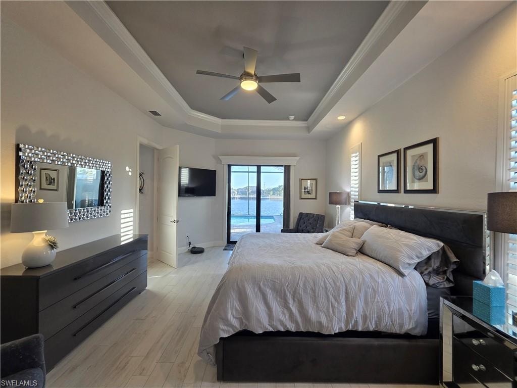Bedroom with access to outside, ornamental molding, light wood-type flooring, a ceiling fan, and a tray ceiling