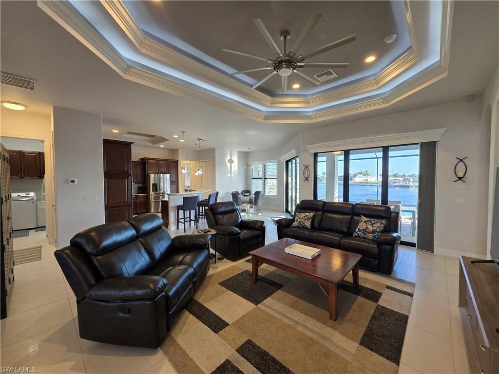 Living area with ornamental molding, ceiling fan, recessed lighting, light tile patterned floors, and a tray ceiling