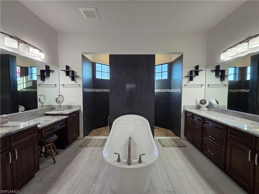 Bathroom featuring a walk in shower, a freestanding bath, healthy amount of natural light, and two vanities