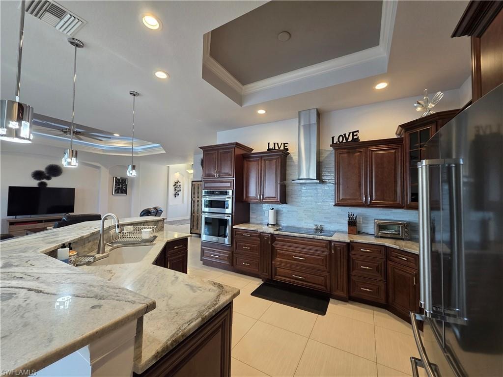Kitchen with a raised ceiling, crown molding, appliances with stainless steel finishes, dark brown cabinetry, and hanging light fixtures