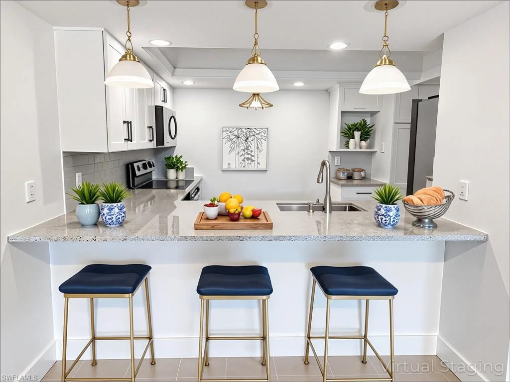 Kitchen featuring a peninsula, a kitchen bar, light stone countertops, appliances with stainless steel finishes, and recessed lighting
