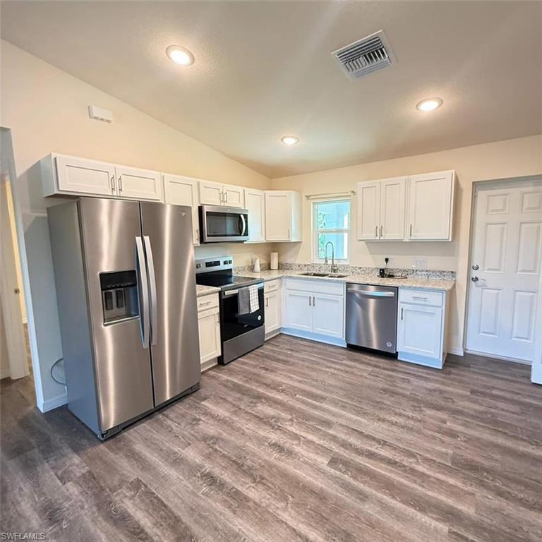 Kitchen featuring stainless steel appliances, white cabinetry, vaulted ceiling, dark wood finished floors, and recessed lighting