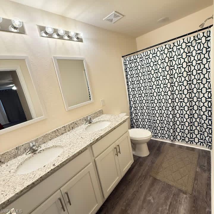 Full bath with double vanity, dark wood-type flooring, and curtained shower