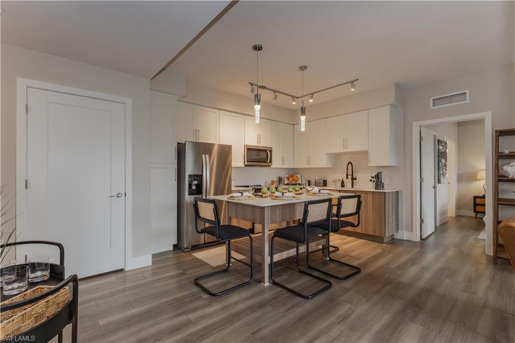 Kitchen featuring stainless steel appliances, white cabinetry, light countertops, hanging light fixtures, and dark wood-style floors
