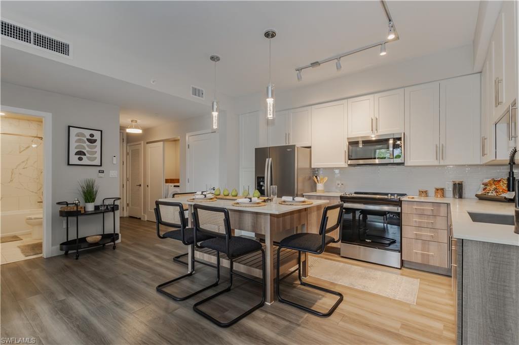 Kitchen with appliances with stainless steel finishes, light wood finished floors, pendant lighting, and light stone counters