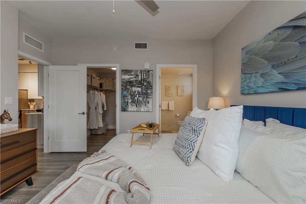 Bedroom with a spacious closet, wood finished floors, connected bathroom, and a ceiling fan