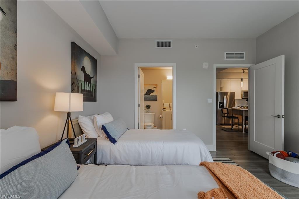 Bedroom featuring stainless steel fridge with ice dispenser, dark wood finished floors, and connected bathroom
