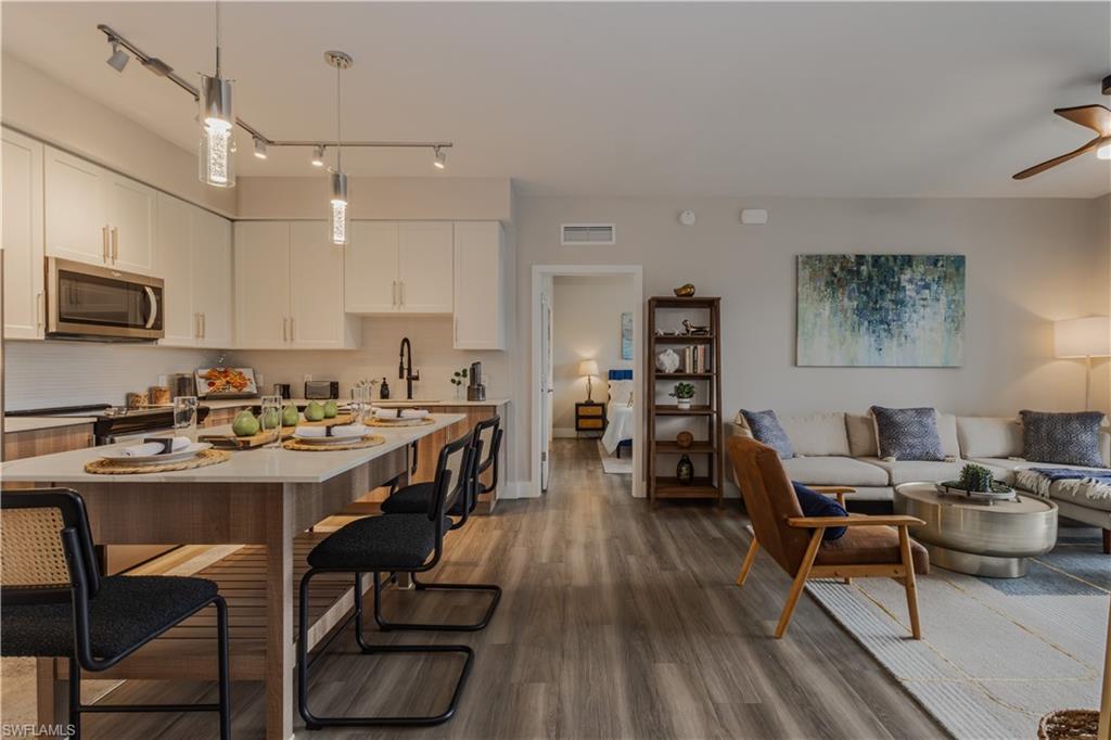 Kitchen with open floor plan, a kitchen bar, stainless steel appliances, dark wood-style floors, and white cabinetry