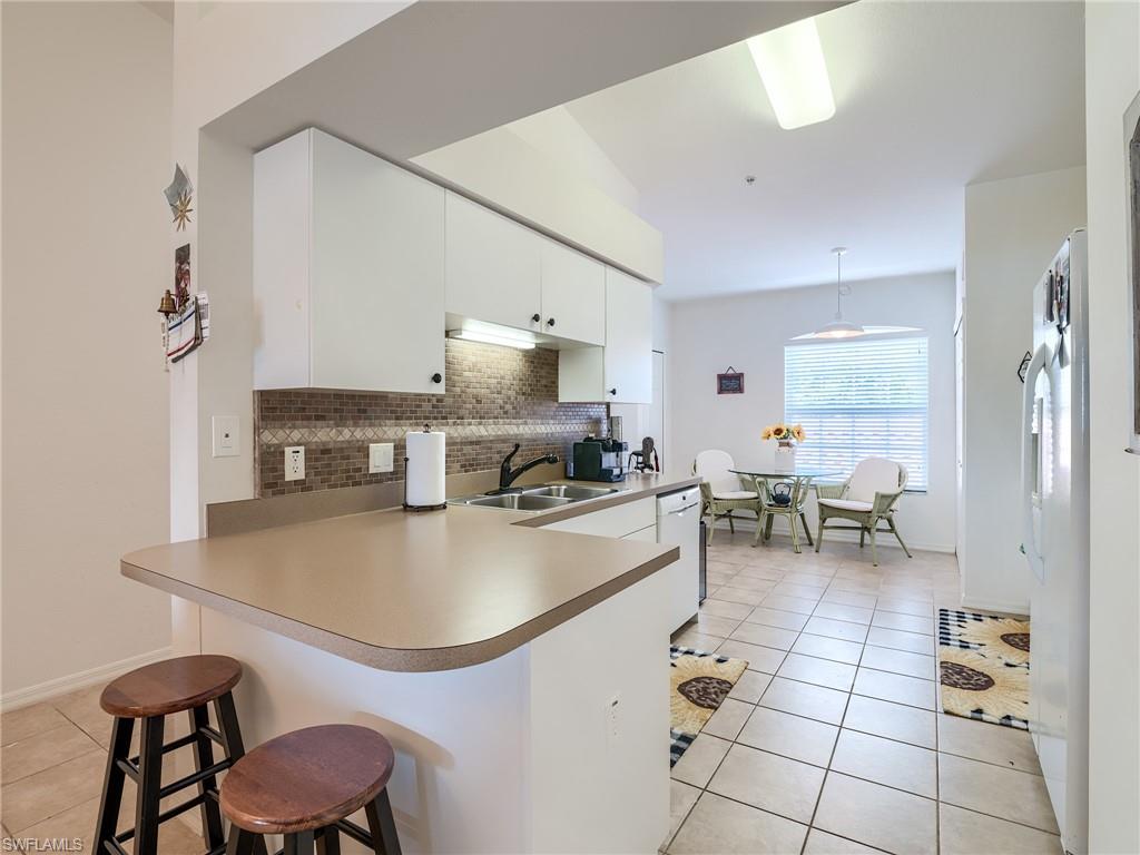 Kitchen with a peninsula, a kitchen breakfast bar, light tile patterned floors, decorative light fixtures, and decorative backsplash