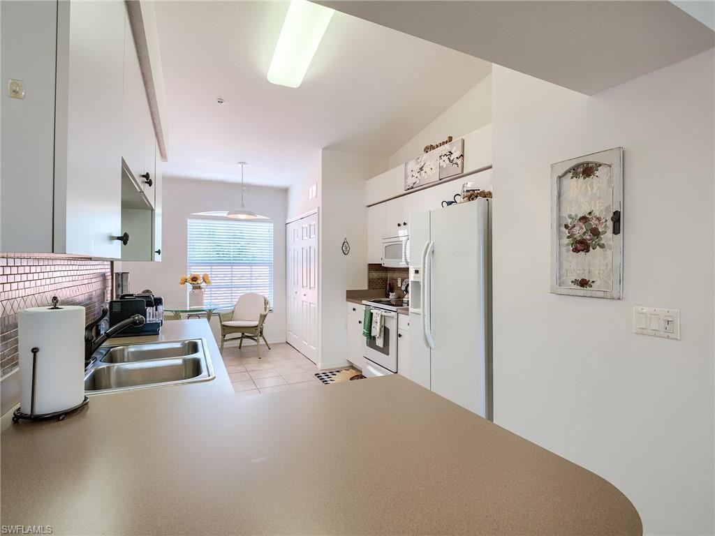 Kitchen featuring decorative backsplash, white appliances, white cabinetry, pendant lighting, and a peninsula