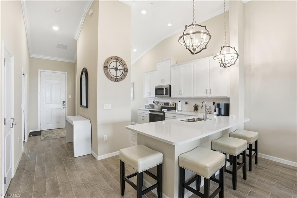 Kitchen with stainless steel appliances, a kitchen bar, white cabinetry, wood tiled floors, and decorative backsplash