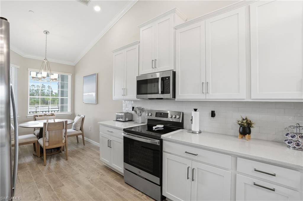Kitchen featuring stainless steel appliances, crown molding, white cabinets, vaulted ceiling, and hanging light fixtures
