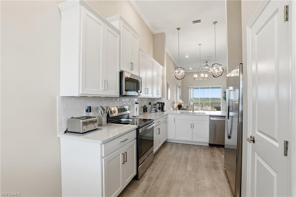Kitchen with stainless steel appliances, white cabinetry, decorative light fixtures, backsplash, and light wood finished floors