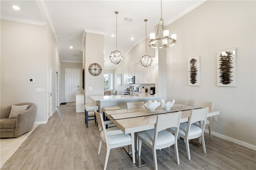 Dining area with wood finish floors, a chandelier, crown molding, a high ceiling, and recessed lighting