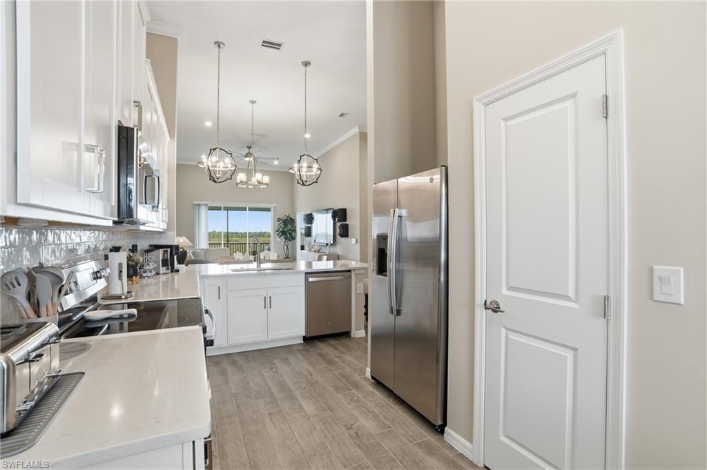 Kitchen featuring white cabinetry, stainless steel appliances, ornamental molding, decorative light fixtures, and light stone countertops