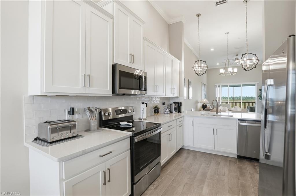 Kitchen featuring stainless steel appliances, white cabinetry, light stone countertops, tasteful backsplash, and crown molding