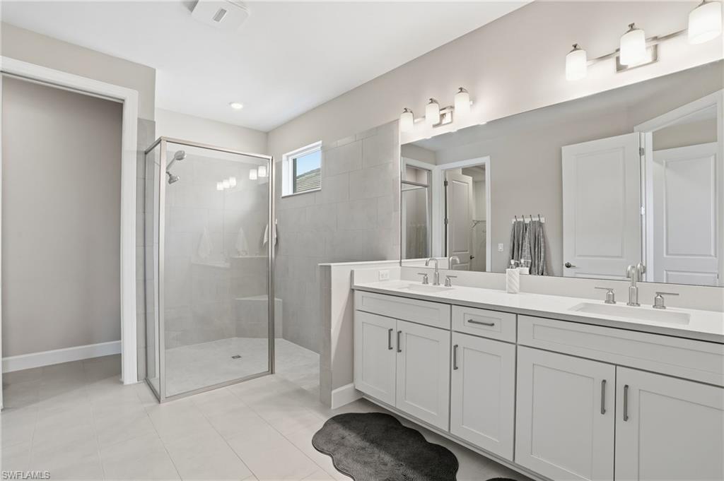 Bathroom featuring double vanity, a shower stall, and light tile patterned floors