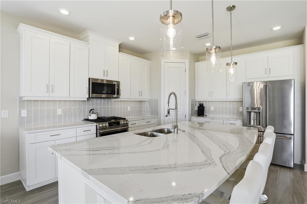 Kitchen with high quality appliances, light stone countertops, white cabinets, and recessed lighting