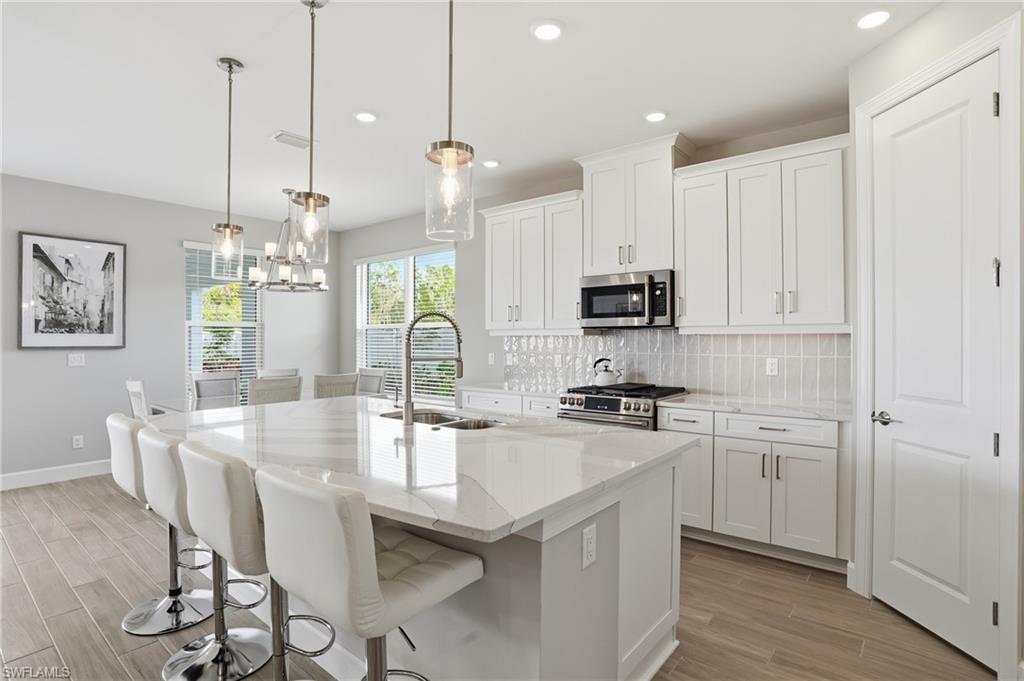 Kitchen with light stone countertops, wood tiled floors, a kitchen breakfast bar, white cabinets, and recessed lighting