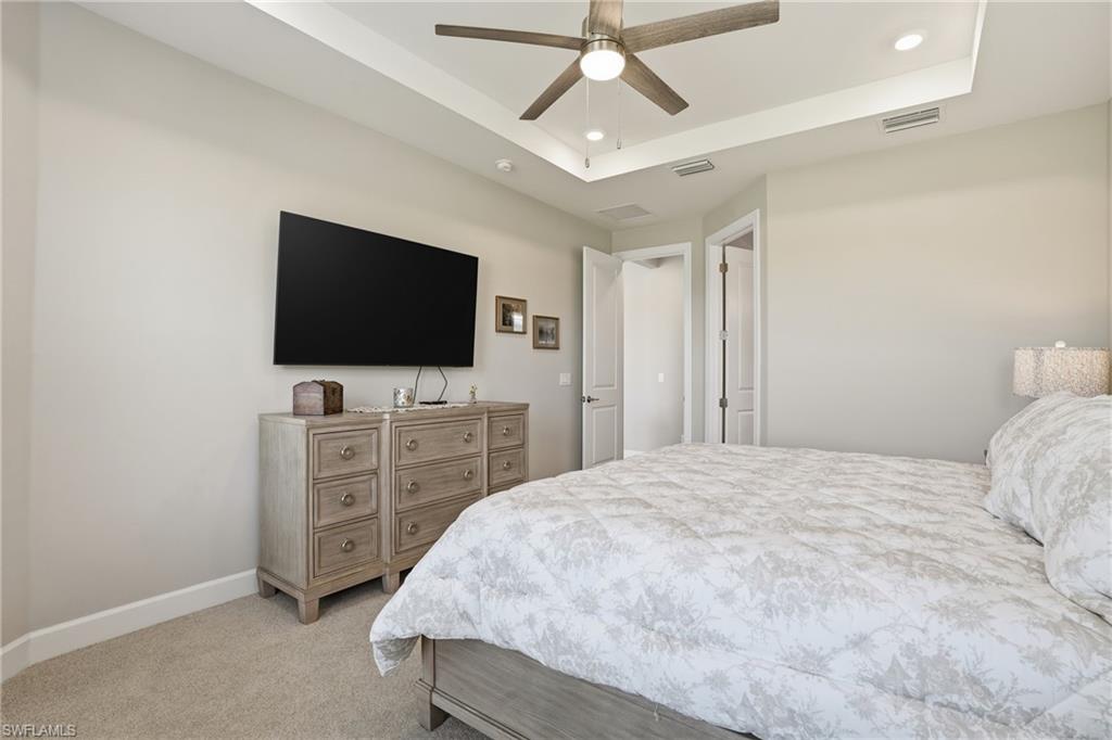 Bedroom featuring light colored carpet, ceiling fan, a tray ceiling, and recessed lighting