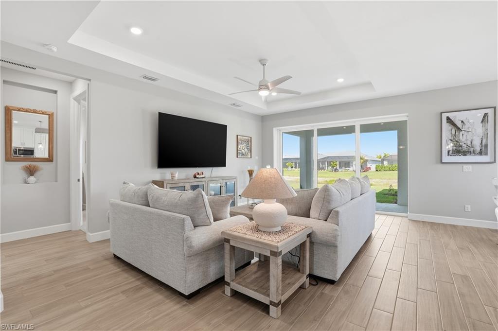 Living area with a tray ceiling, light wood-style flooring, a ceiling fan, and recessed lighting