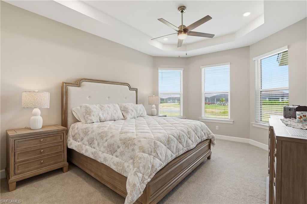 Bedroom with light colored carpet, a raised ceiling, ceiling fan, and recessed lighting