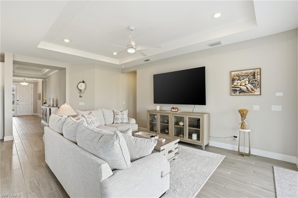 Living room featuring a tray ceiling, wood finish floors, ceiling fan, and recessed lighting