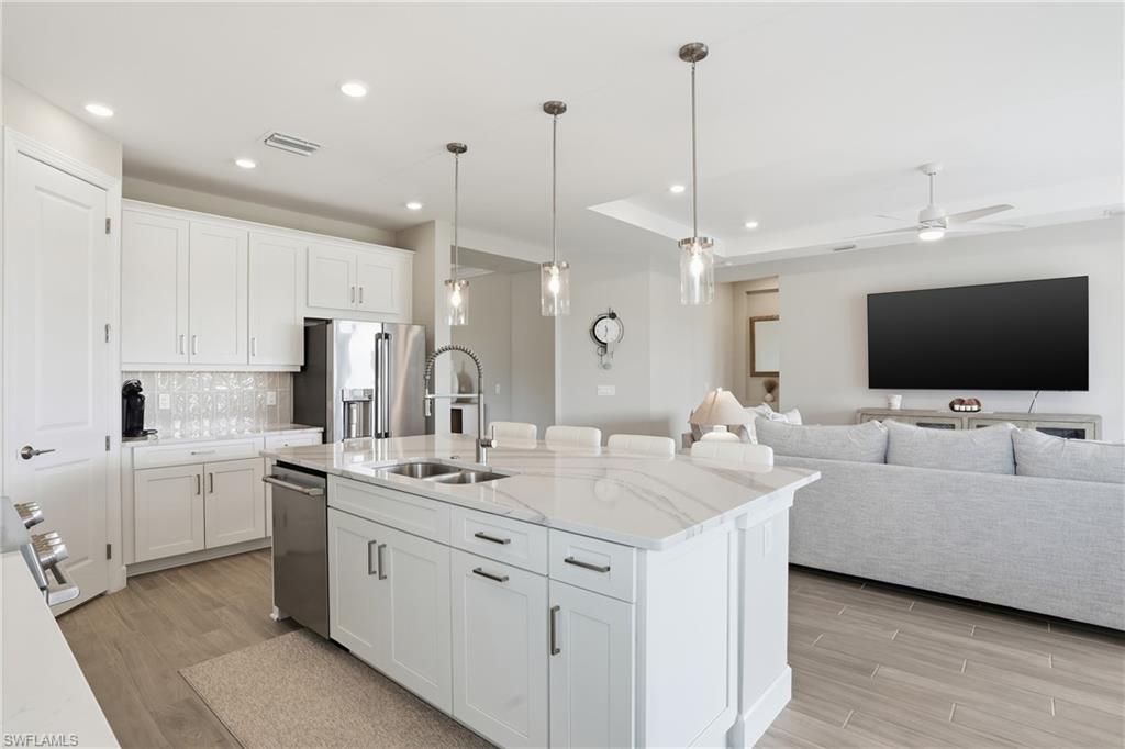 Kitchen featuring white cabinetry, decorative light fixtures, a center island with sink, light stone countertops, and recessed lighting