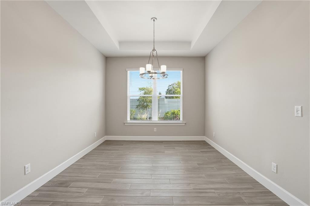 Unfurnished dining area with wood tiled floors, a chandelier, and a tray ceiling