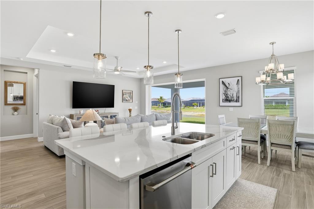 Kitchen with white cabinetry, stainless steel dishwasher, a center island with sink, light wood-style floors, and light stone counters