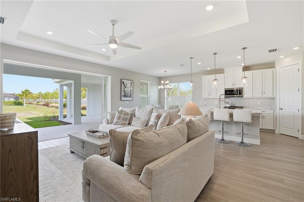 Living room with a chandelier, light wood-style floors, a ceiling fan, a raised ceiling, and recessed lighting