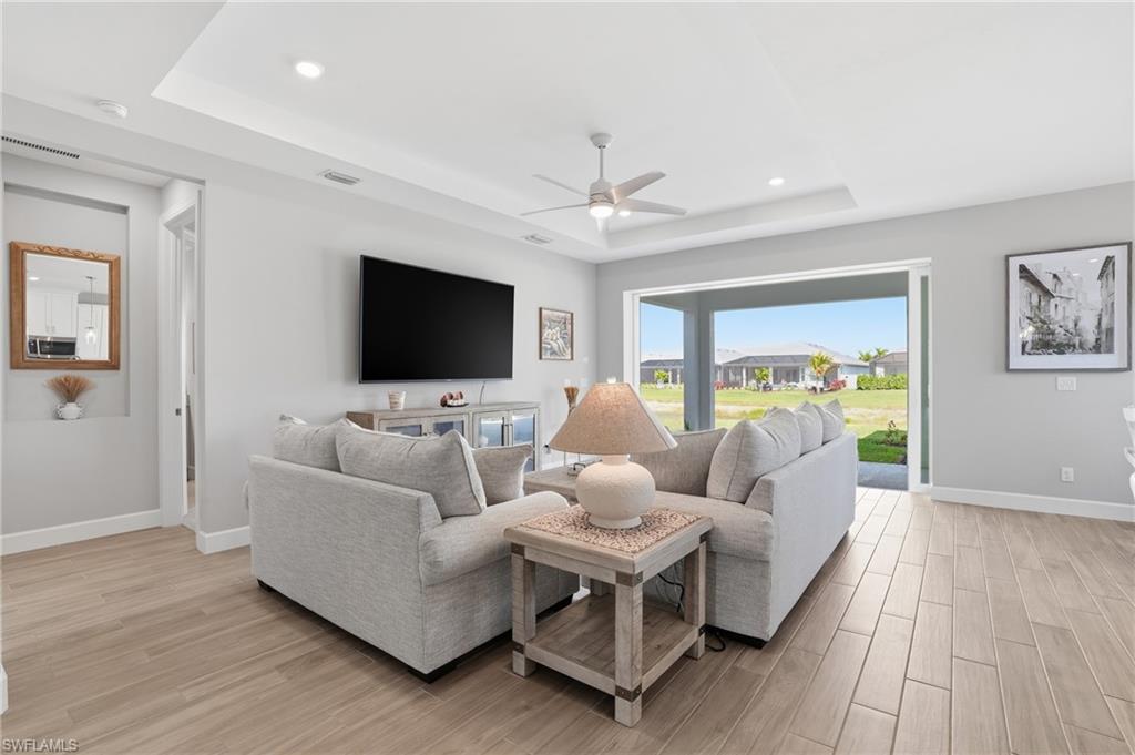 Living area featuring a tray ceiling, light wood-type flooring, ceiling fan, and recessed lighting