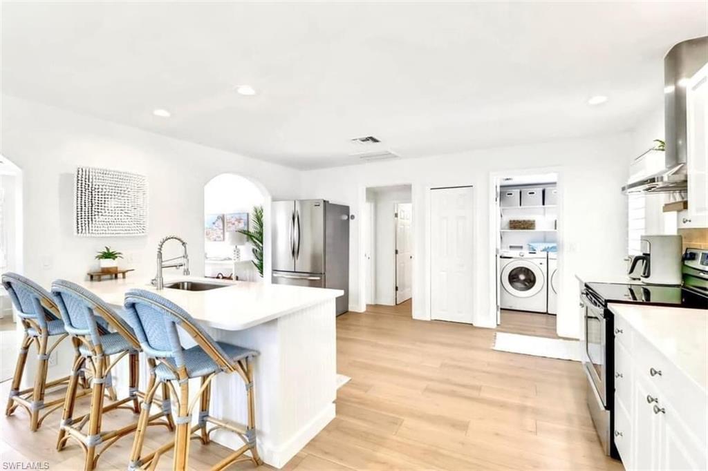 Kitchen featuring white cabinetry, sink, stainless steel appliances, washing machine and dryer, and light hardwood / wood-style flooring