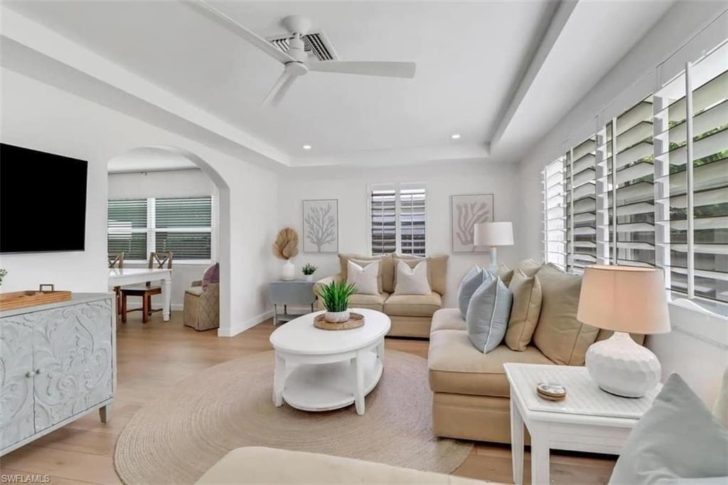 Living room featuring a tray ceiling, a healthy amount of sunlight, ceiling fan, and light hardwood / wood-style floors